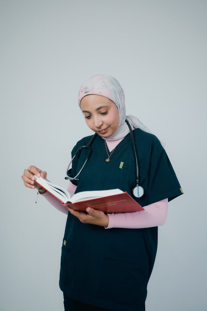 Medical professional in scrubs reading a book with focus and concentration.